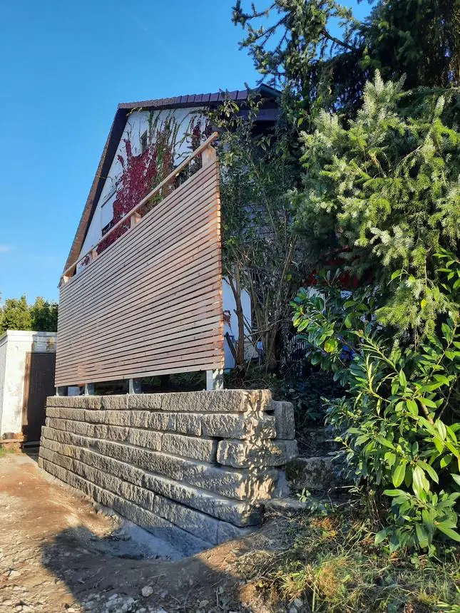 Sichtschutz aus waagerechten Holzlatten auf einer Natursteinmauer vor einem Wohnhaus
